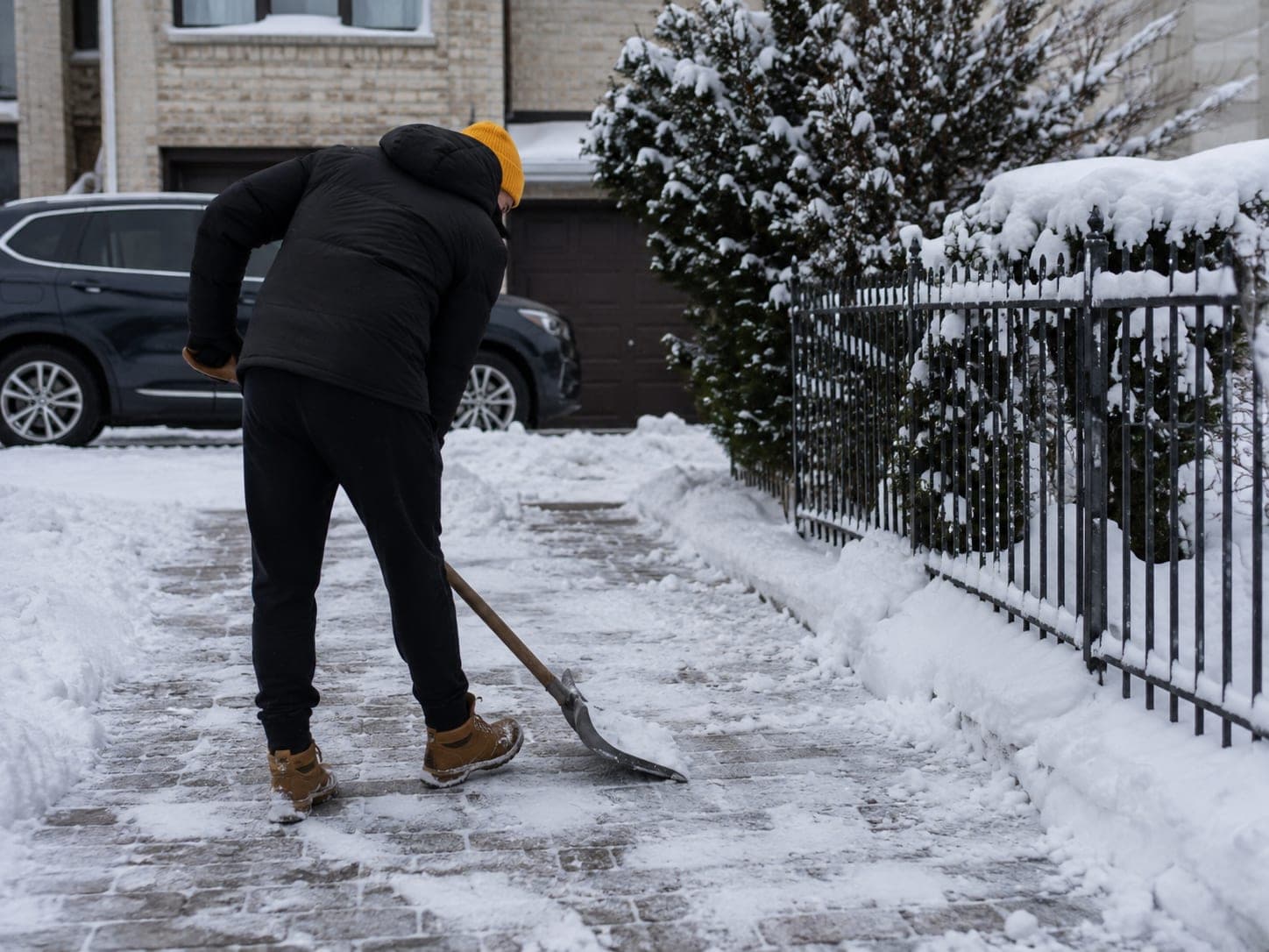 Winterdienst: Räumen eines schneebedeckten Gehwegs vor einem Wohnhaus